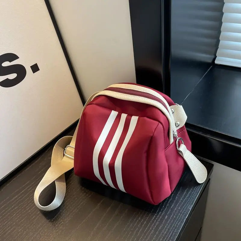 Borsa a tracolla rossa con strisce bianche, design moderno, chiusura a zip, ideale per moda casual. Accessorio elegante e funzionale.