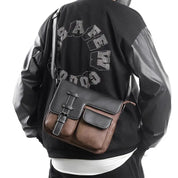 Borsa a tracolla in pelle nera e marrone, indossata su giacca nera con maniche in pelle. Design elegante, ideale per moda urbana e casual.