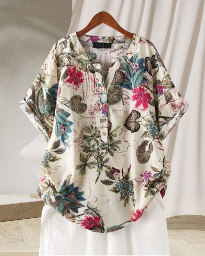Camicia donna floreale in cotone, maniche corte, colletto a V, bottoni, sfondo bianco, design casual estivo, appesa su gruccia di legno.