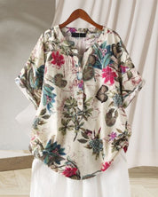 Camicia donna floreale in cotone, maniche corte, colletto a V, bottoni, sfondo bianco, design casual estivo, appesa su gruccia di legno.