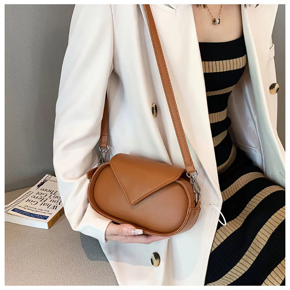 Donna con borsa a tracolla in pelle marrone, indossa abito a righe nero e beige e cappotto bianco. Accessorio moda elegante e versatile.