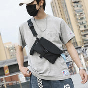 Giovane con mascherina indossa t-shirt grigia e borsa a tracolla nera in città. Moda urbana, accessori uomo, stile casual.