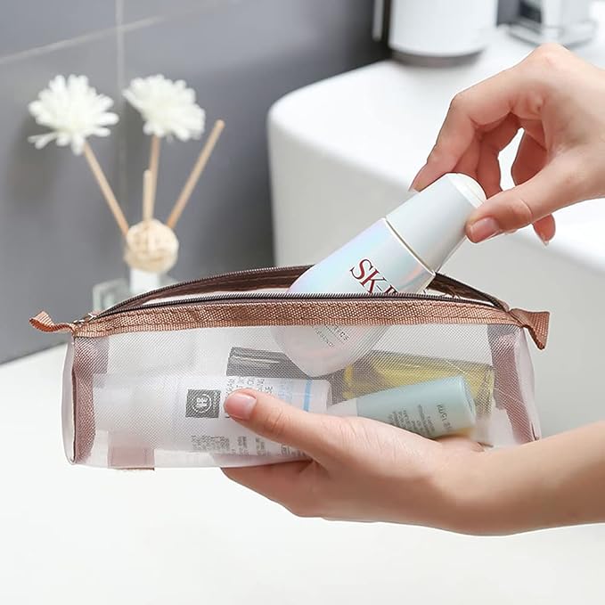 Mani che inseriscono cosmetici in una pochette trasparente da viaggio, bagno moderno sullo sfondo. Organizzatore trucco, accessori da viaggio.