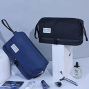Due beauty case da viaggio, uno blu e uno nero, con zip e manico, su sfondo grigio. Accessori da bagno inclusi: rasoio, crema, profumo.