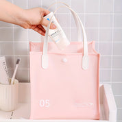Borsa da viaggio rosa in PVC con manici bianchi, ideale per cosmetici. Design elegante, impermeabile, perfetta per organizzare prodotti da bagno.