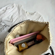 Abito bianco su sfondo chiaro con borsa beige aperta contenente tablet rosa, bottiglia marrone, portafoglio e accessori. Moda casual elegante.