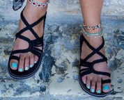Sandali intrecciati neri su piedi femminili con smalto turchese, cavigliere colorate. Scarpe estive eleganti, moda donna, accessori boho.