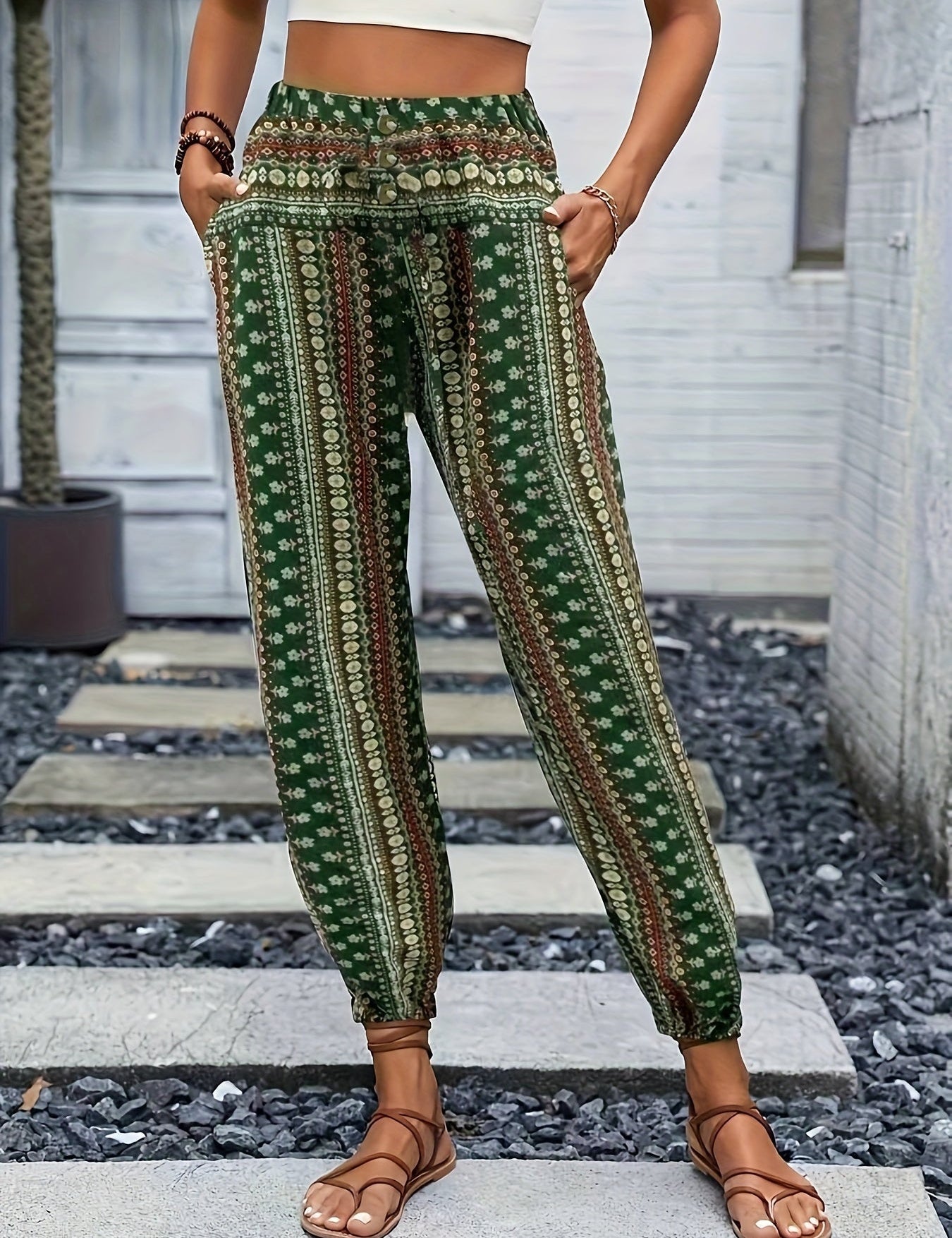 Pantaloni boho verdi a righe floreali, vita alta, tasche laterali, indossati con sandali marroni. Stile casual estivo per donna.