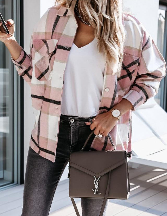 Donna con camicia a quadri rosa, t-shirt bianca, jeans neri e borsa a tracolla marrone con logo. Look casual chic, moda autunnale.