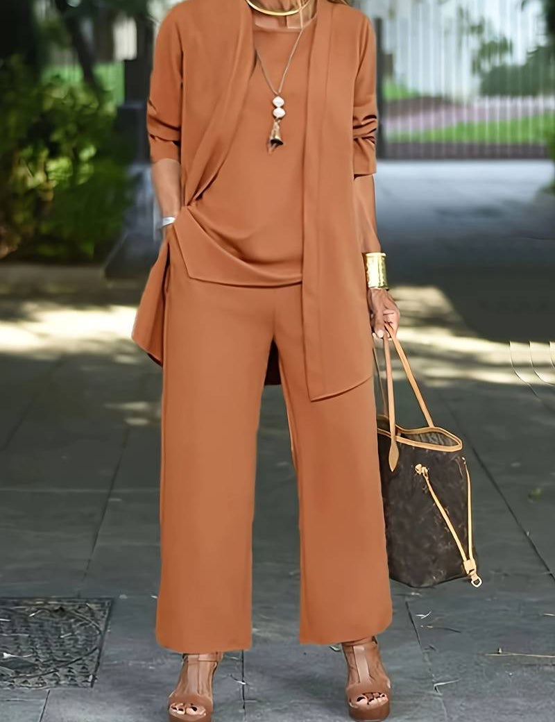 Completo donna elegante marrone, giacca lunga e pantaloni larghi, borsa a tracolla di lusso, sandali con tacco, bracciale dorato. Moda autunnale chic.