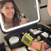 Donna che si trucca davanti a uno specchio illuminato, con beauty case aperto contenente vari cosmetici. Trucco, specchio LED, beauty case organizzato.