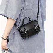 Borsa a tracolla nera in pelle, design elegante con fibbie argentate, indossata su abito a quadri. Accessorio moda donna, stile casual chic.