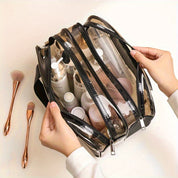 Borsa trasparente per cosmetici con zip, contenente flaconi di prodotti skincare e pennelli trucco. Ideale per organizzare e trasportare accessori beauty.