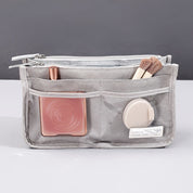 Organizer da borsa grigio con tasche multiple, contenente pennelli trucco, specchietto e rossetto. Accessorio pratico per organizzazione borsa.