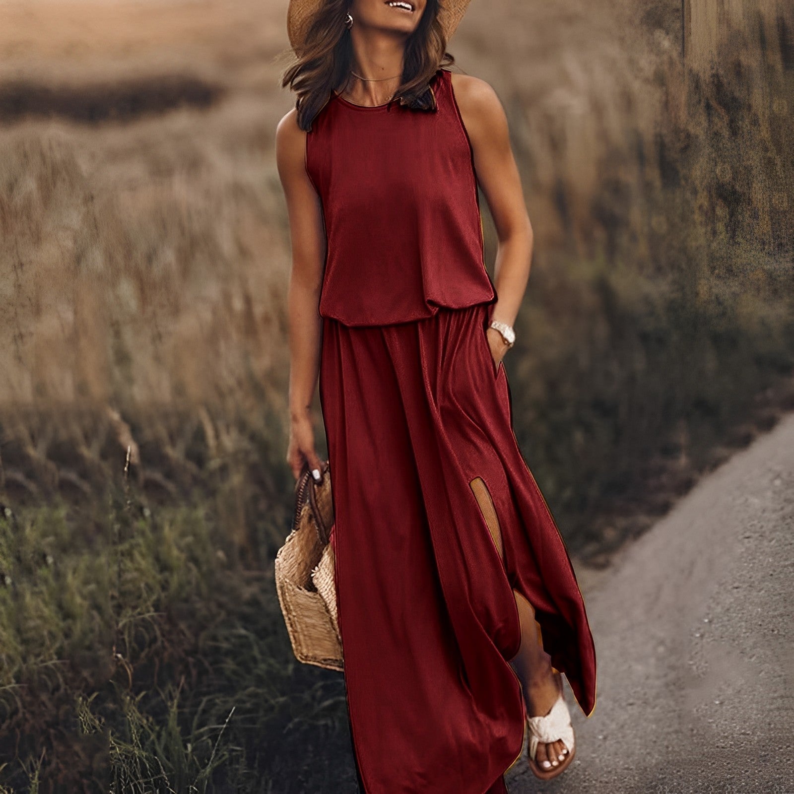 Donna con abito lungo rosso estivo, cappello di paglia e borsa intrecciata, cammina su un sentiero. Moda estiva, abbigliamento casual elegante.