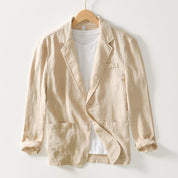 Giacca beige in lino su gruccia, con tasche frontali e maniche arrotolate, abbinata a t-shirt bianca. Elegante e casual, ideale per moda estiva.