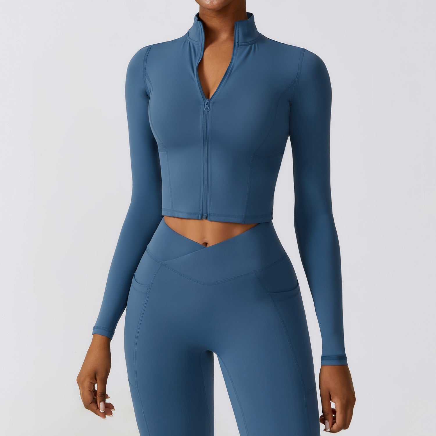 Donna in abbigliamento sportivo blu, top a maniche lunghe con zip e leggings a vita alta. Outfit fitness elegante e moderno per yoga o palestra.
