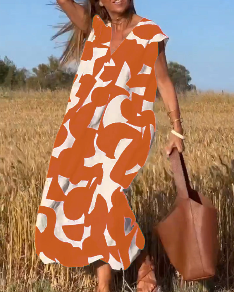 Abito estivo lungo con stampa astratta arancione e bianca, indossato da una donna in un campo di grano, borsa in pelle marrone, giornata soleggiata.