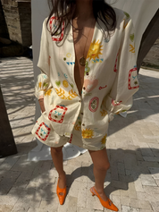 Donna con camicia oversize stampata con motivi colorati e scarpe arancioni su pavimento in pietra. Moda estiva, abbigliamento casual chic.