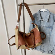 Borsa a tracolla in tela beige e pelle marrone su appendiabiti accanto a giacca di jeans. Accessori moda casual, stile urbano.