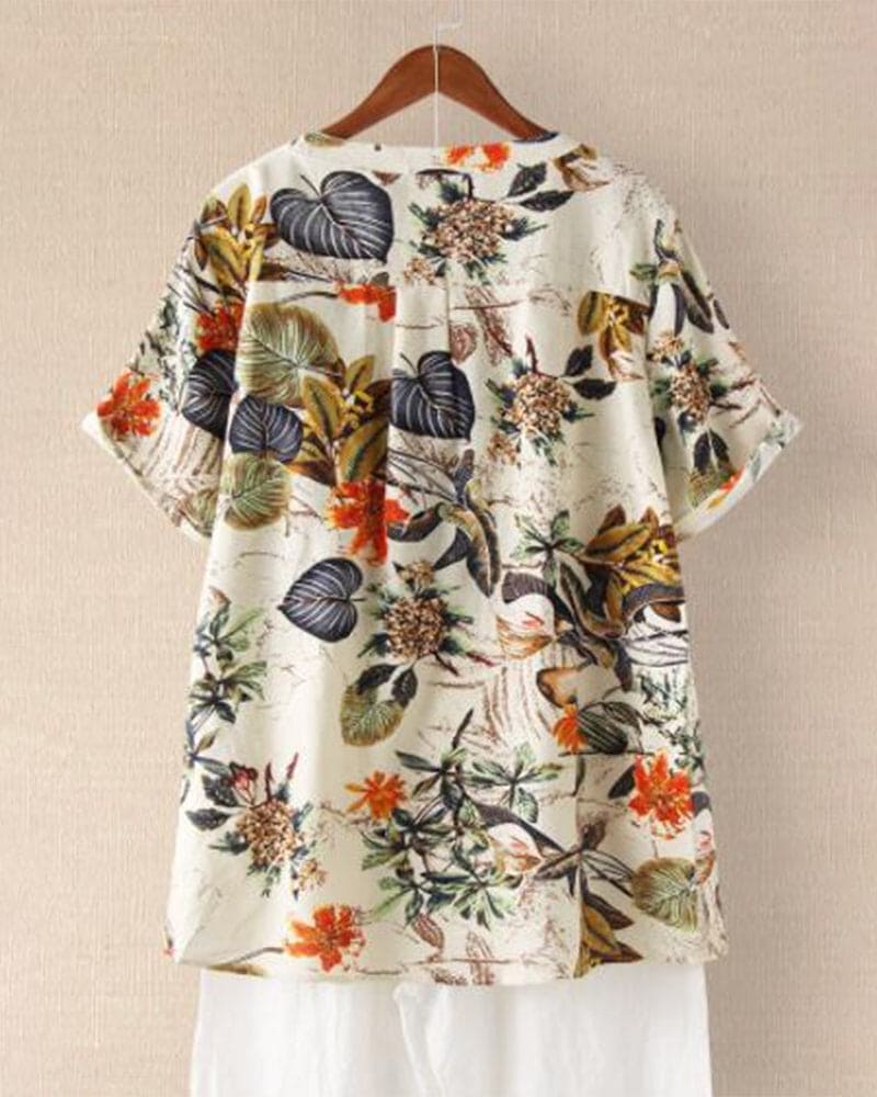 Camicia estiva da donna con stampa floreale tropicale, maniche corte, sfondo beige, colori vivaci, casual e leggera, perfetta per la stagione calda.