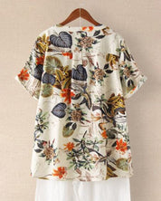 Camicia estiva da donna con stampa floreale tropicale, maniche corte, sfondo beige, colori vivaci, casual e leggera, perfetta per la stagione calda.