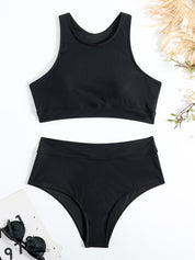 Costume da bagno nero a due pezzi, top sportivo e slip a vita alta, su sfondo bianco con occhiali da sole e decorazioni floreali.