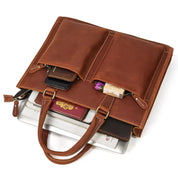 Borsa in pelle marrone con tasche esterne, contenente laptop, smartphone e passaporto. Elegante e funzionale per lavoro e viaggio.