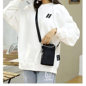 Donna con felpa bianca e jeans, indossa una borsa a tracolla nera. Stile casual, moda urbana, accessori pratici per tutti i giorni.