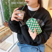 Donna con felpa nera e jeans, tiene una borsa a scacchi verde e bianca e un bicchiere di caffè. Stile casual, moda autunnale, accessori trendy.