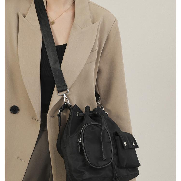 Giacca beige elegante con borsa a tracolla nera in nylon, design moderno, chiusura con zip, ideale per moda urbana e look casual chic.