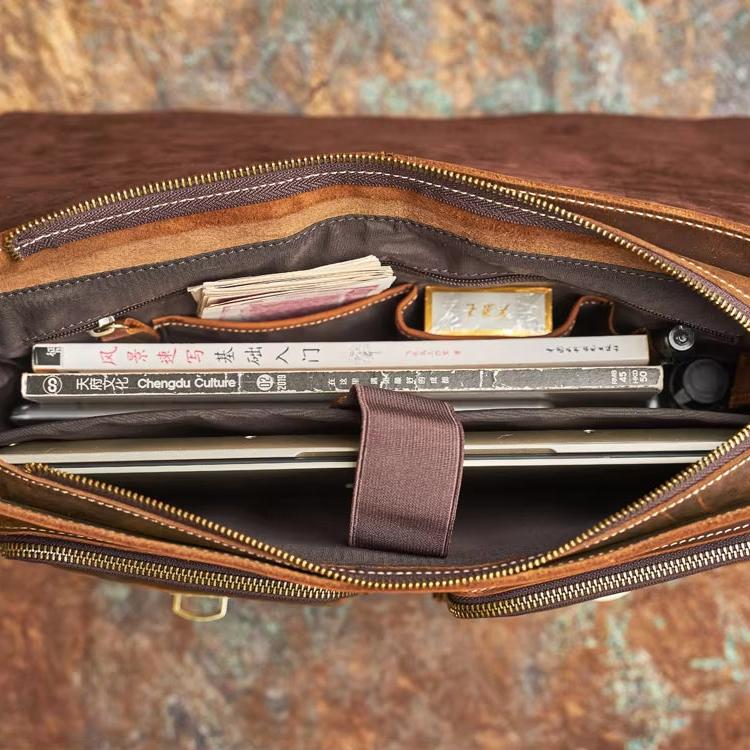 Borsa in pelle marrone aperta, vista dall'alto, con libri, quaderni e laptop all'interno. Accessorio elegante per lavoro e studio.