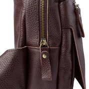 Zaino in pelle marrone scuro con texture granulosa, cerniera dorata e tasca laterale. Design elegante e resistente, ideale per viaggi e lavoro.