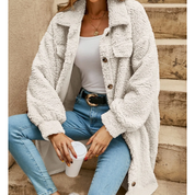 Donna con cappotto teddy bianco, jeans attillati e cintura nera, tiene una tazza da caffè. Moda autunnale casual, stile urbano chic.