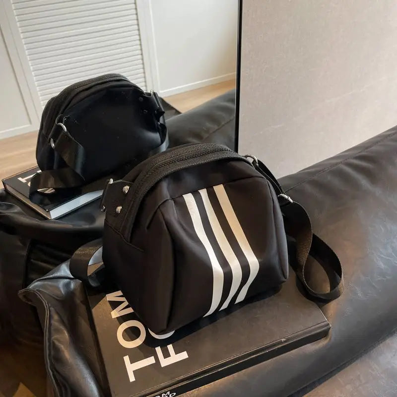 Zaino nero con strisce bianche riflettenti, posizionato su un libro su un divano nero. Design moderno, ideale per moda urbana e viaggi.
