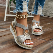 Sandali estivi da donna con zeppa, cinturino in tessuto grigio, dettaglio dorato, suola in corda, abbinati a jeans strappati. Moda casual elegante.