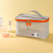 Borsa cosmetica in rete grigia con cerniera arancione, manico superiore, su sfondo giallo. Accessori trucco accanto. Organizzatore da viaggio elegante.