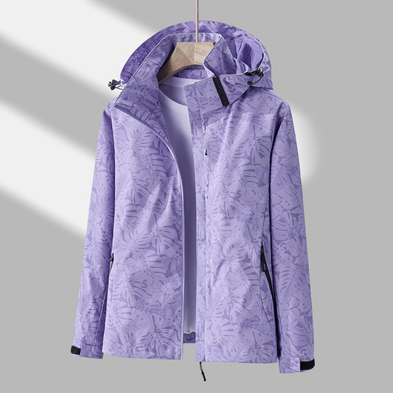 Giacca impermeabile viola con cappuccio, motivo foglie, chiusura zip, tasche laterali, ideale per outdoor e sport. Abbigliamento donna autunno.