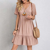 Abito estivo donna in cotone beige, maniche corte, scollo a V, con borsa a tracolla in paglia. Look casual elegante per moda estiva.