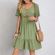Abito estivo verde donna, maniche corte, scollo a V, tessuto leggero, accessoriato con borsa a tracolla in paglia. Moda casual elegante.