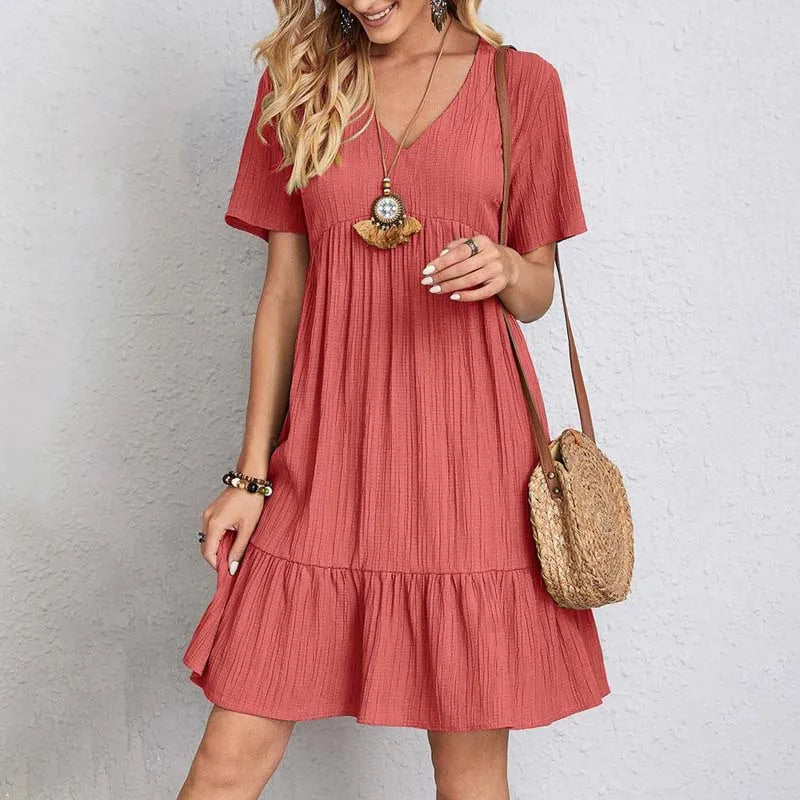 Abito estivo donna rosso corallo, maniche corte, scollo a V, tessuto leggero, accessoriato con borsa a tracolla in paglia. Moda casual estiva.