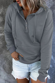 Donna con felpa grigia con cappuccio e bottoni, tasca frontale, abbinata a shorts di jeans chiari. Look casual e moderno.