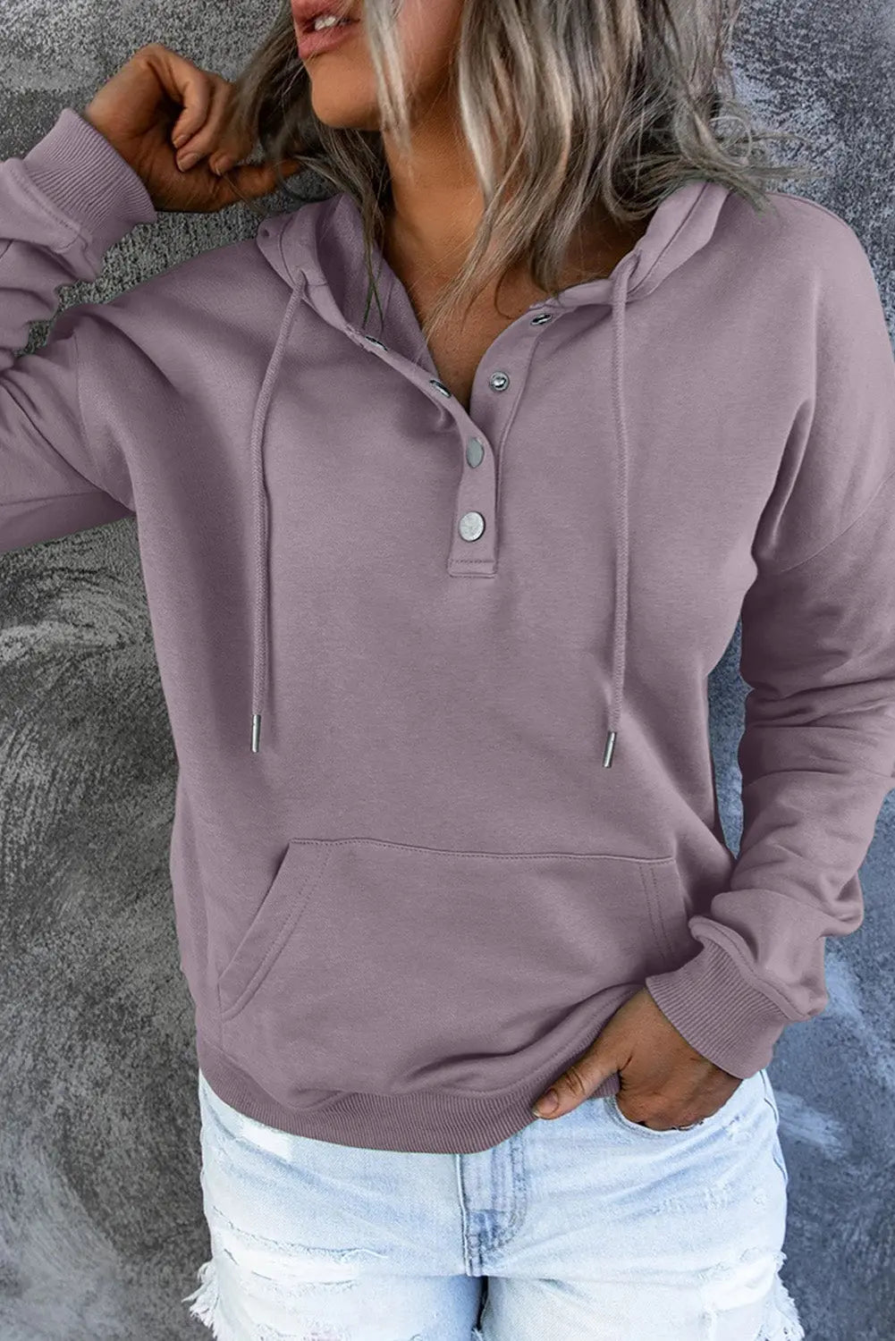 Felpa con cappuccio da donna, colore lavanda, con bottoni e tasca frontale, abbinata a jeans strappati. Look casual e moderno.