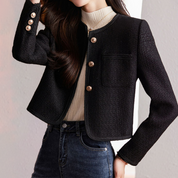Giacca donna elegante nera in tweed con bottoni dorati, abbinata a maglia beige e jeans a vita alta. Moda autunno inverno, stile casual chic.