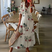 Donna con abito lungo floreale bianco, borsa di paglia, in sala da pranzo moderna. Moda estiva, abbigliamento casual elegante, arredamento interno.