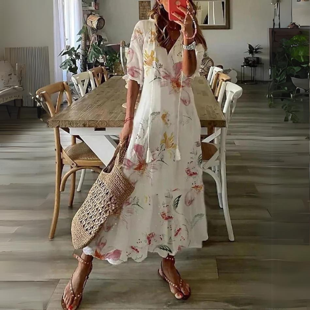 Donna con abito lungo floreale bianco, sandali e borsa di paglia in una sala da pranzo moderna. Moda estiva, abbigliamento casual elegante.