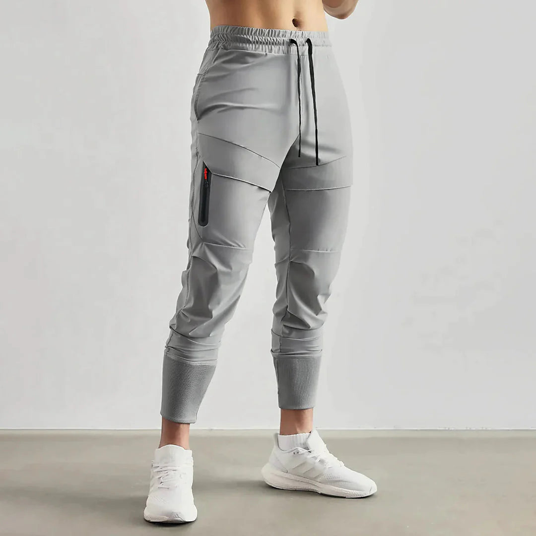 Pantaloni sportivi grigi da uomo, design moderno con tasca laterale, elastico in vita e caviglie, ideali per fitness e tempo libero.