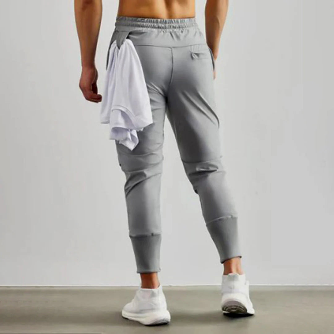 Pantaloni sportivi grigi da uomo, vestibilità slim, con tasche posteriori, abbinati a scarpe da ginnastica bianche e maglietta bianca.