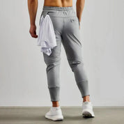Pantaloni sportivi grigi da uomo, vestibilità slim, con tasche posteriori, abbinati a scarpe da ginnastica bianche e maglietta bianca.