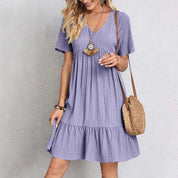 Abito estivo donna viola, maniche corte, scollo a V, tessuto leggero, borsa a tracolla in paglia, moda casual, look estivo elegante.